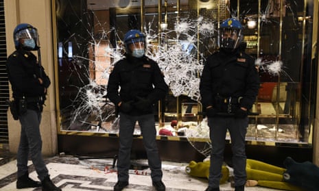 Italian police officers stand in front of a shattered Gucci store window in Turin during a protest against coronavirus restrictions.