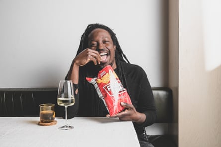 Chef Paul Carmichael is sitting at a table with a glass of white wine, eating out of a packet of French fries