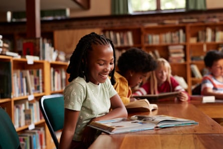 Happy girl reading book in libraryHappy girl reading book while sitting at table in library at elementary school