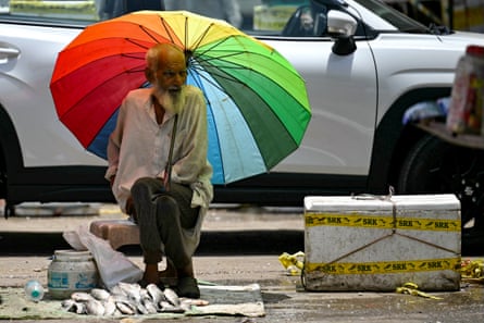 Man taking shade under a milticoloured umbrella with a pile fish on the ground at his feet