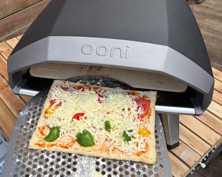 Rectangular vegetable pizza being slid into the Ooni Koda 2 pizza oven, while outdoors on a wooden table.