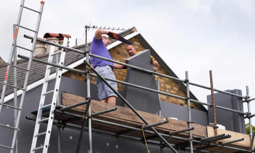 Workers attach foam wall-insulation panels to a terraced house.