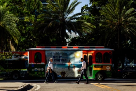 Two people walk in front of a colorful trolley bus.