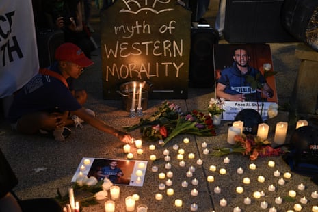 Small candles are lit at a makeshift shrine to an Al Jazeera journalist, whose picture is sat next to the candles. A sign reads “myth of western morality”.