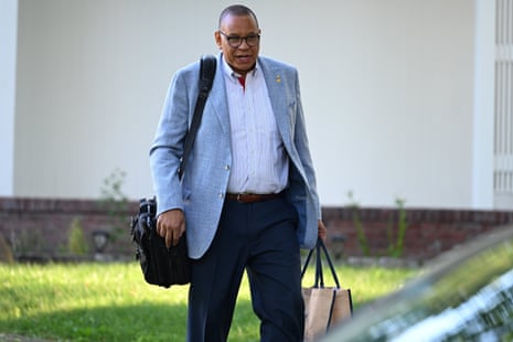 Lieutenant Governor Dale Caldwell, in a grey blazer, walks outside carrying bags, smiling