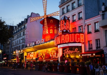 Tourists stand in front of the Moulin Rouge lit up at night