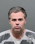 tattooed man in striped shirt looks ahead in mugshot