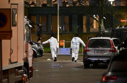 Two police officials in white crime scene suits walk away carrying a heavy box