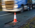 Lorry passing large cone marking giant pothole on country road.