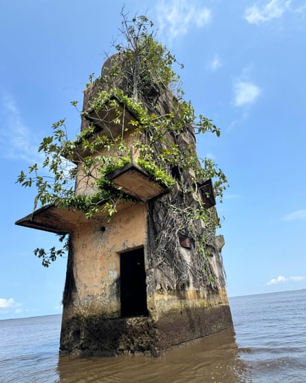 Abandoned concrete tower with vines growing on it. It is now surrounded by river water as it sinks into the ground