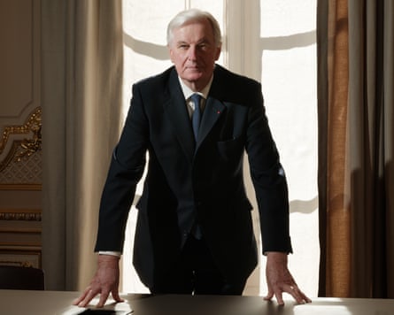 Michel Barnier stands at a table and presses his hands on to its surface with his fingers splayed