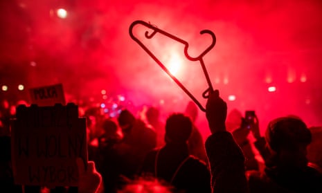 A protester holds up a coat hanger against a background of red flares