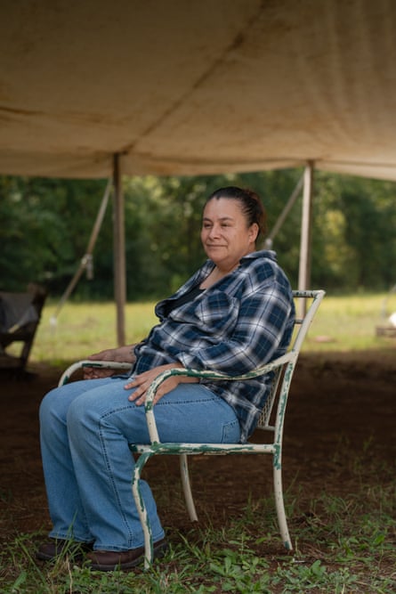 woman in blue plaid shirt and jeans sits outside on chair under tent smiling