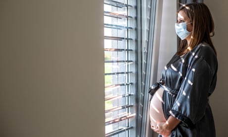 Young pregnant woman with medical face mask looking out of window