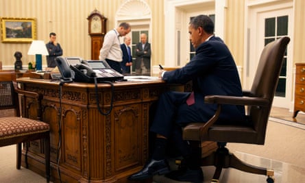 Obama sits at the Resolute Desk in the Oval Office. Joe Biden is among those in attendance.