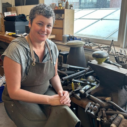 Rebecca Joselyn, a silversmith, sits in her workshop surrounded by tools, wearing an apron.