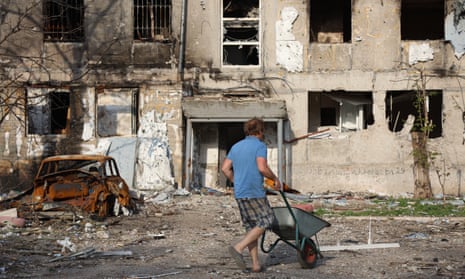 Man pushes wheelbarrow in front of bomb-damaged building