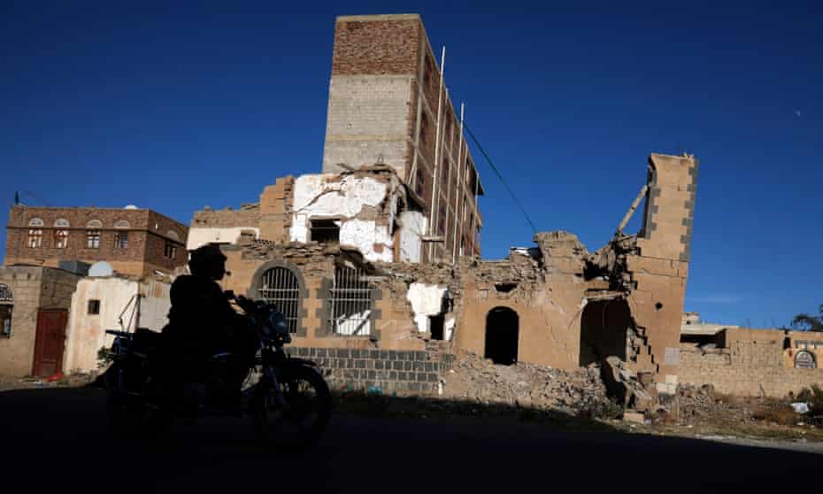 A motorcyclist drives past a destroyed building in Sana’a