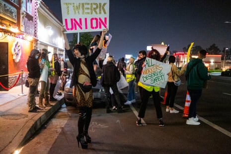 A group of dancers stand on the street outside a club holding signs that say 'Twerk Union' and 'All workers deserve safety'.