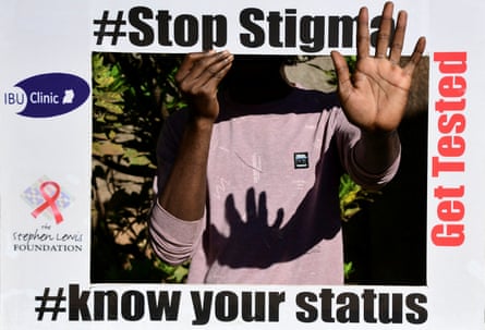 A person hold a placard obscuring their face that reads, ‘Spot stigma. Know your status. Get tested’.