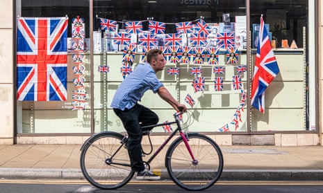 cyclist rides past shop window full of jubilee flags