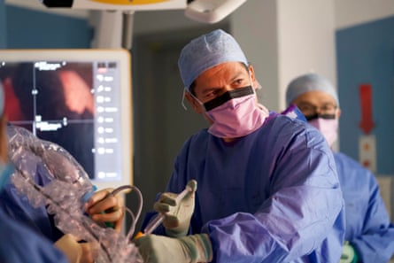 A surgeon in scrubs and a face mask holding a syringe
