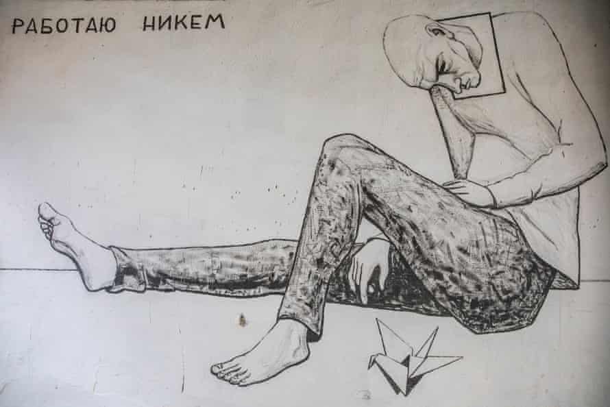 Black and white artwork of a man sitting on the floor with his leg extended, looking down toward the ground at an origami bird next to him