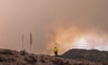 Single man in yellow shirt seen from back on top of hill looking at clouds of smoke.