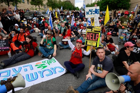 A group of around fifty people protest with flags and signs on a street in Israel