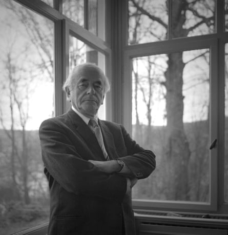 black and white photo of a man in a suit with his arms crossed posing by a window