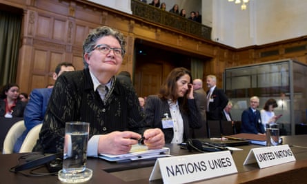 Elinor Hammarskjold waits to speak at the International Court of Justice; she has short grey hair and glasses and wears a white shirt with dark jacket.