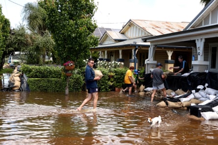 People carrying sandbags through brown flood waters in front of a house