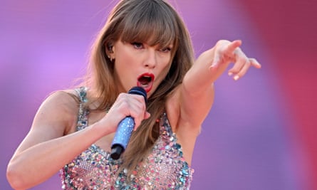 Taylor Swift points toward the camera, with a microphone to her mouth. 