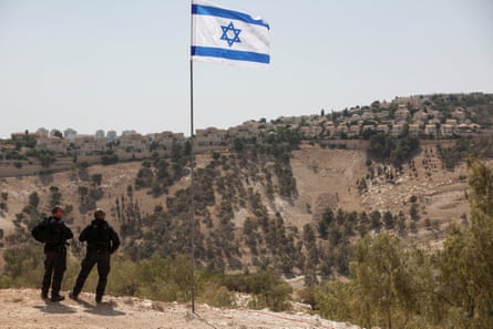 An Israeli flag flutters with an Israeli settlement in the West Bank visible in the background