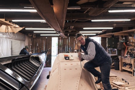 Silvia Scaramuzza in a workshop leaning over the frame of a gondola with an adze tool