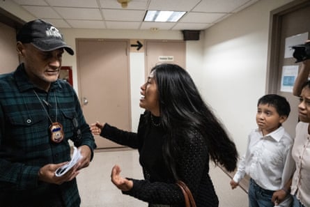a woman pleads with a man holding papers and wearing a badge around his neck