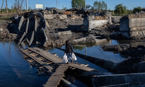 A woman crosses the Bakhmutka River on a makeshift wooden bridge next to a destroyed bridge in Bakhmutka, eastern Ukraine, following Russian attacks