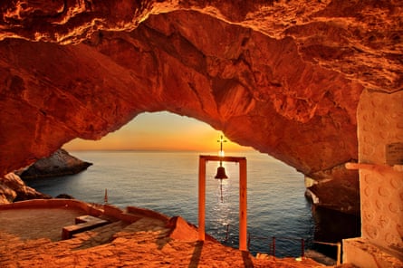 Cave and chapel with bell, lit by colourful sunset across the sea