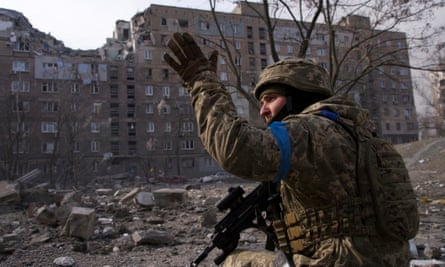 A uniformed Ukrainian serviceman gestures before rubble and a building in Mariupol