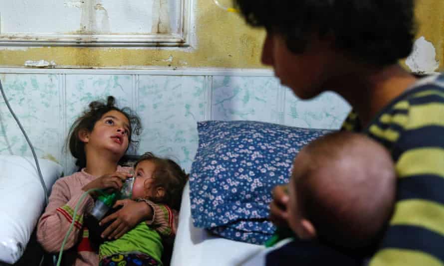Girl leans against wall with young child in her arms. Woman and baby in foreground but out of focus
