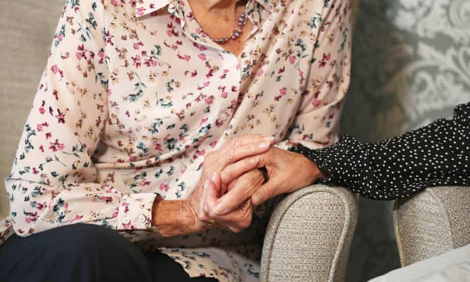 Seated carer holding an elderly woman’s hand