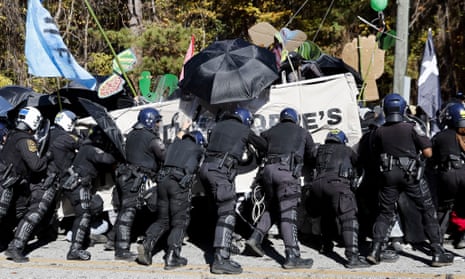 Police officers in riot gear confront demonstrators carrying a banner and protesting at Cop City.