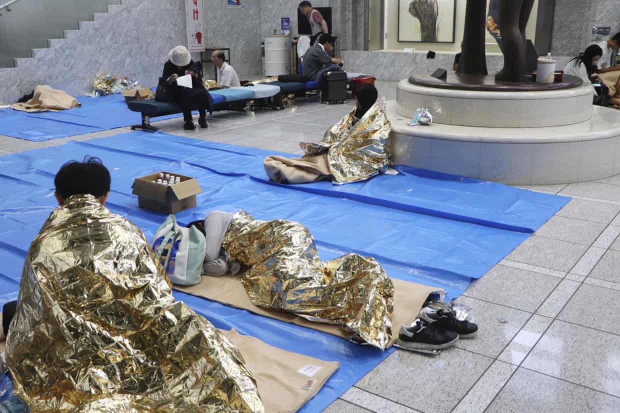 People sleeping on blue matts on the floor of a building’s lobby