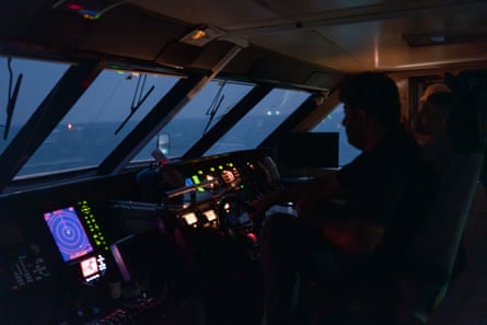 Farouq silhouetted at controls of ferry with sea/sky through windows