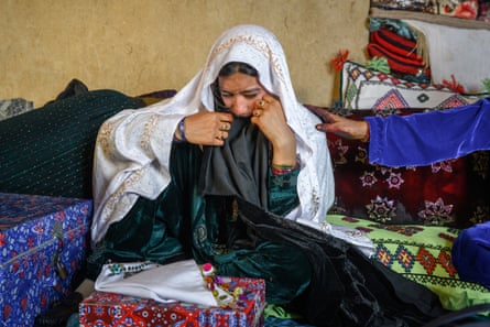 A girl wearing a white head shawl crying. A hand from a woman out of the picture reaches out to comfort her