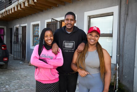 A young African man with his arms round an older woman and with a young woman standing in front of them.