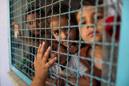 Palestinian children, who fled their homes due to Israeli air and artillery strikes, look through a window fence at a United Nations-run school where they take refuge, in Gaza City.