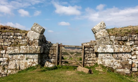Remains of walls and a stone arch, missing the central stones, with a contemporary wooden gate set into it