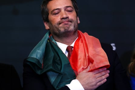 Andre Ventura, with eyes shut, holds his hand to his heart with a Portuguese flag draped around his neck