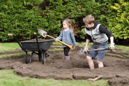 A young girl and a boy digging a wildlife pond in a garden